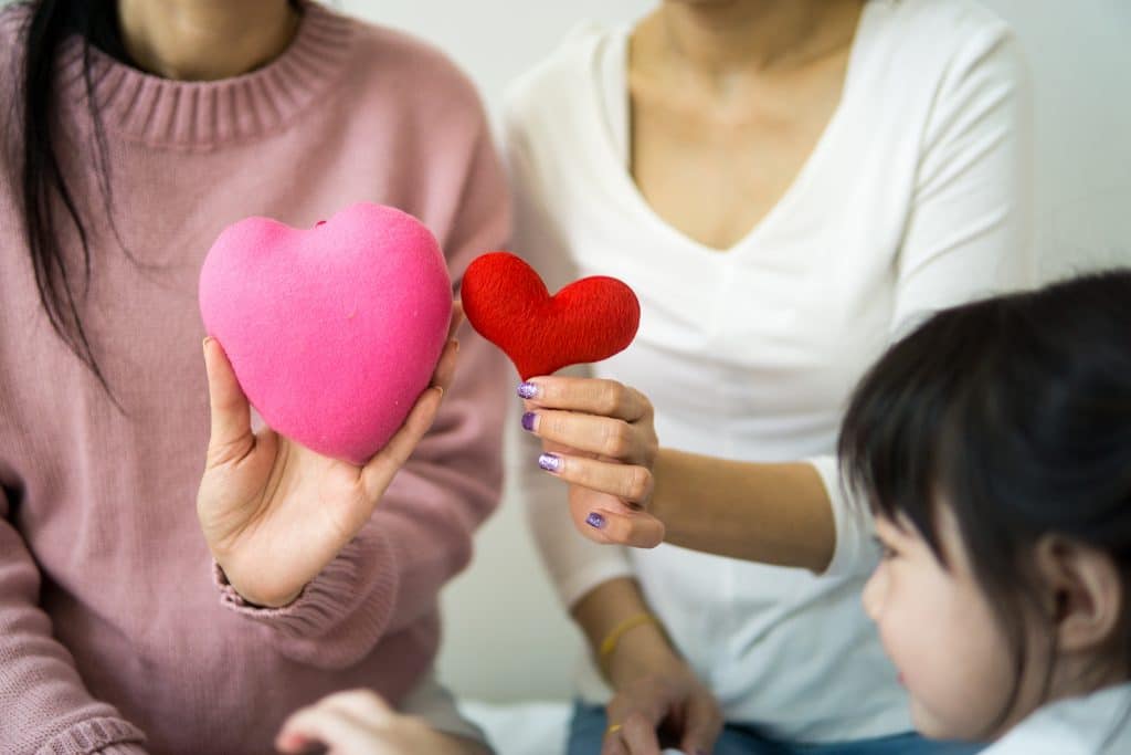 Two women holding plush hearts up in front of a child.